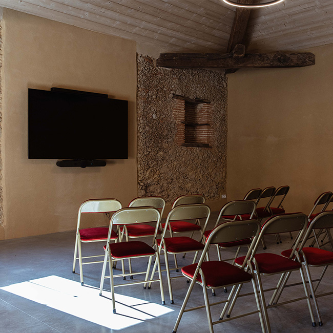Salle de conférence, avec rangées de chaises et télévision.